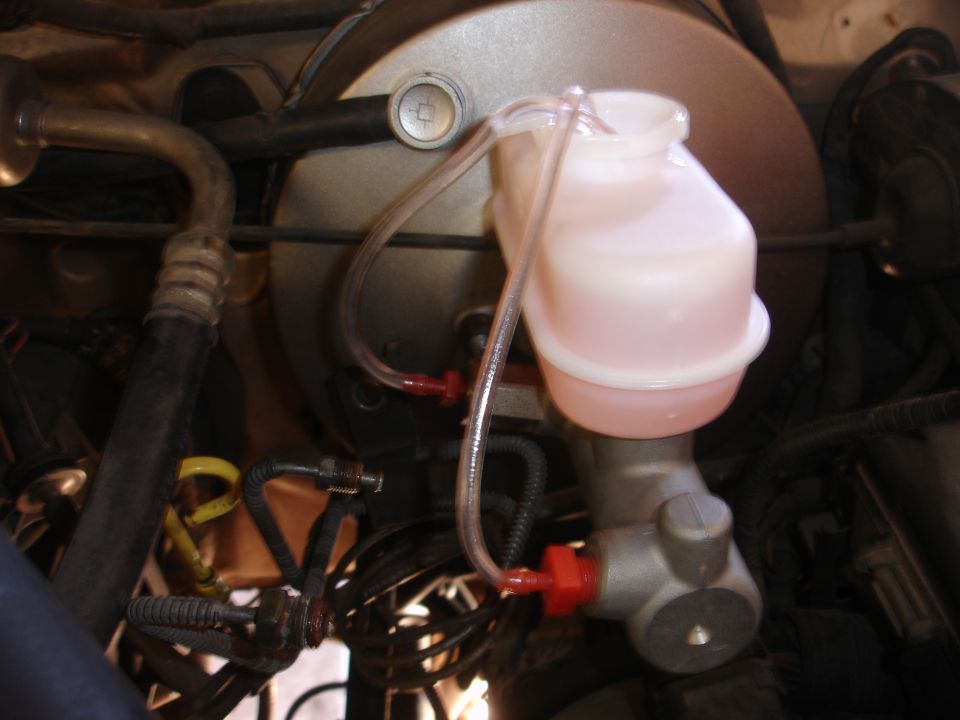 Close-up of a vehicle's master cylinder and brake fluid reservoir with clear tubing attached