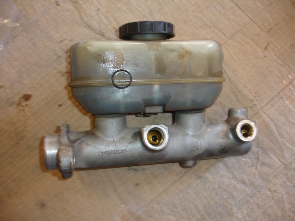 Brake master cylinder with plastic reservoir and metal body. Text on body reads 'TOKICO'