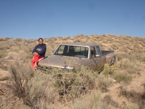 1992 Ford F-350 - A person sits on the hood of a weathered pickup truck partially obscured by desert brush under a clear blue sky.