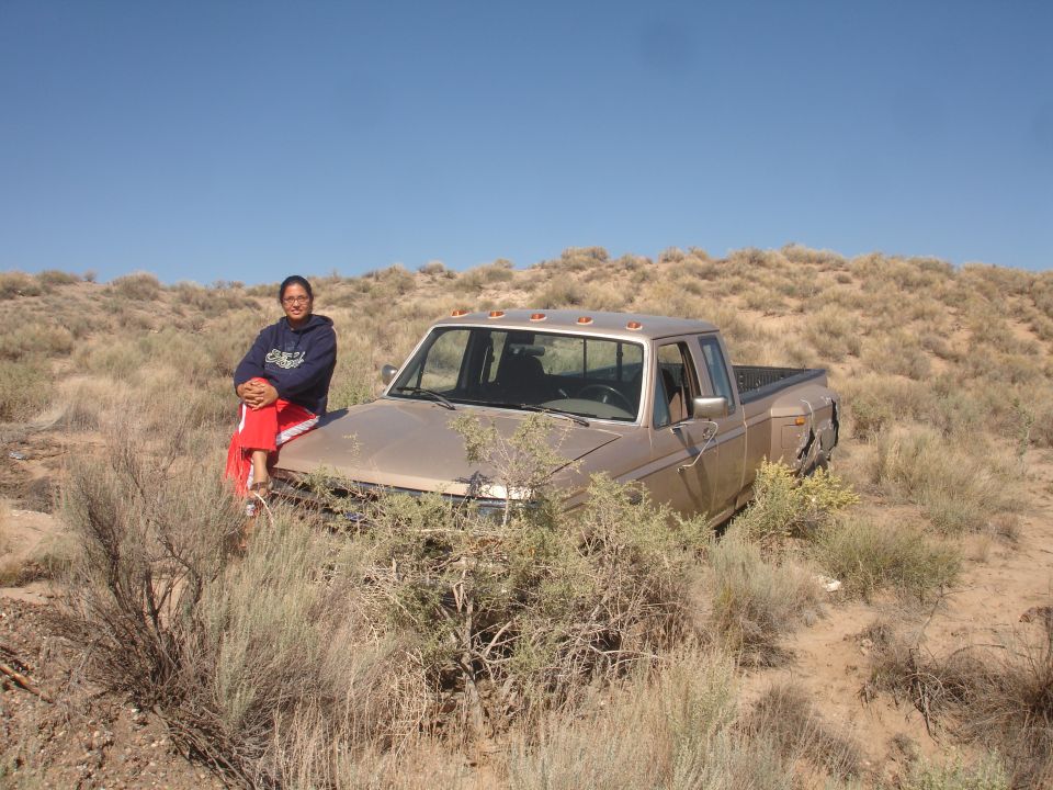 Person sitting on hood of old pickup truck in a dry, brushy area