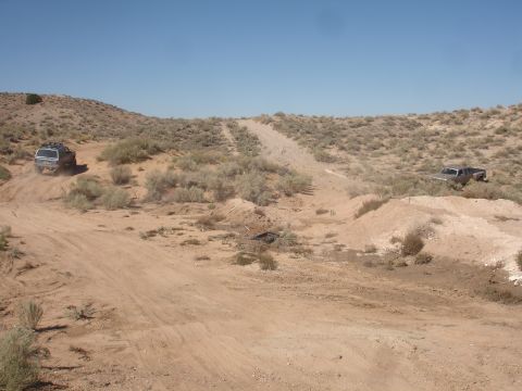 1992 Ford F-350 - Two trucks navigate a dusty off-road trail through a dry, scrub-covered desert landscape.