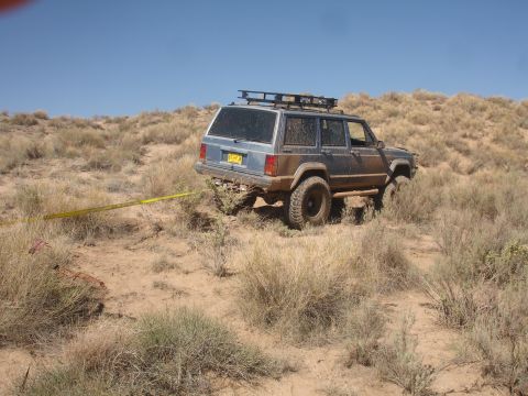 1992 Ford F-350 - A blue Jeep Cherokee XJ is stuck in a dry, brushy terrain with a yellow tow strap attached.