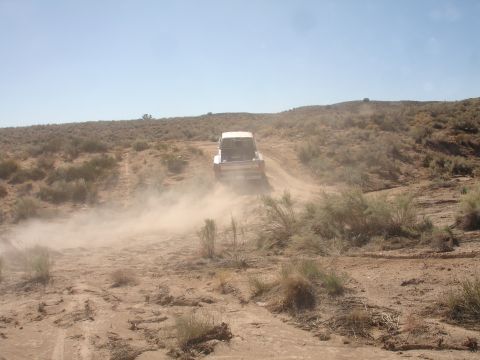 1992 Ford F-350 - Truck driving on a dusty dirt road in a desert landscape. The vehicle is kicking up a lot of dust.