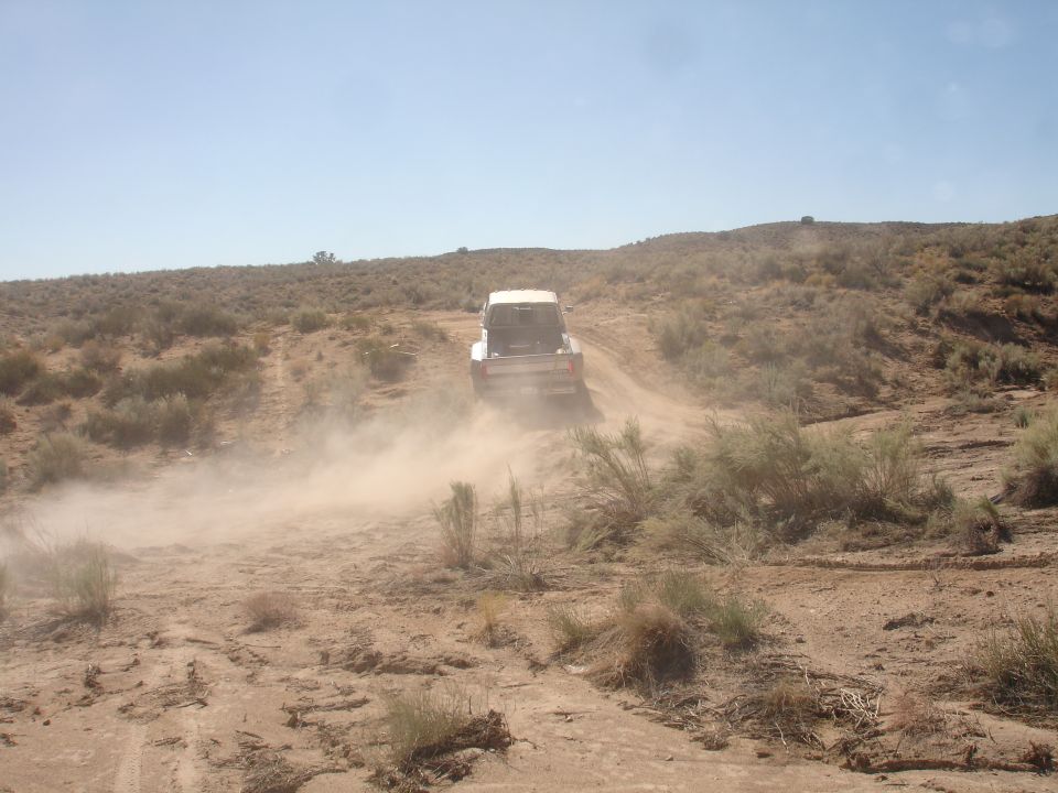 1992 Ford F-350 driving away on a dusty dirt road in a desert landscape