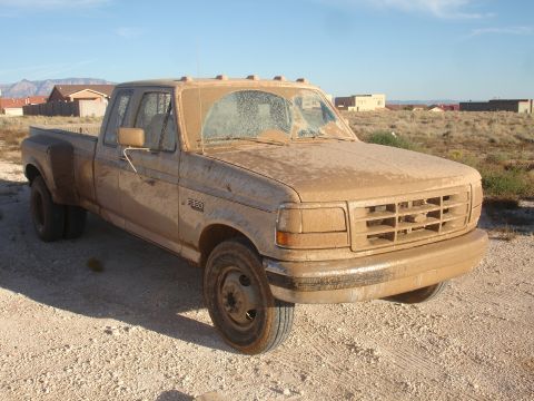 1992 Ford F-350 - This 1992 Ford F-350 dually pickup truck is covered in mud, parked on a dirt road with houses in the background.