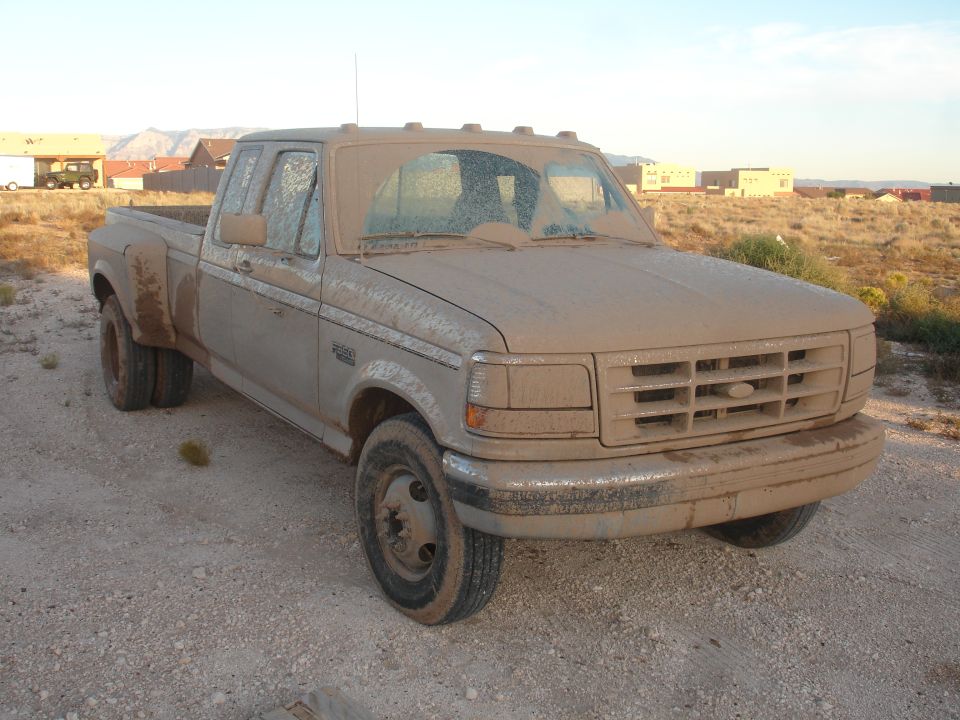 Mud-covered 1992 Ford F-350 dually truck parked on a dirt road