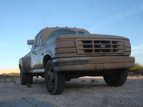 1992 Ford F-350 - A muddy Ford F-350 dually truck sits on a dirt lot under a clear blue sky.