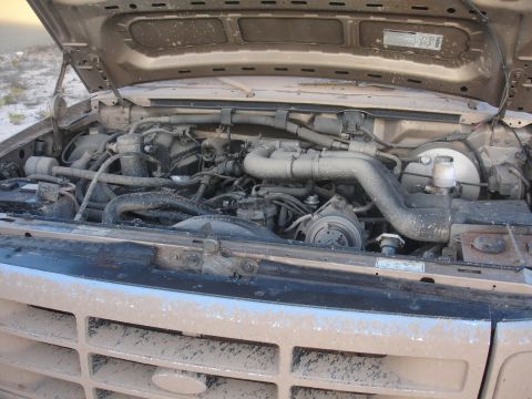 1992 Ford F-350 - The engine bay of a dusty 1992 Ford F-350 is visible with the hood up.