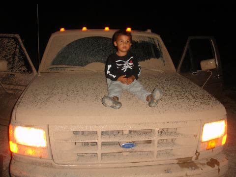 1992 Ford F-350 - A child sits on the hood of a dusty Ford truck at night, with another truck partially visible.