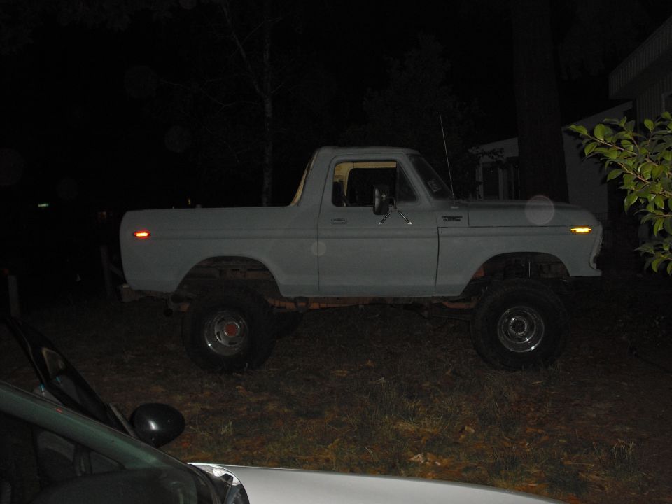 Side view of a light-colored Ford Bronco with a lifted suspension, parked outdoors at night