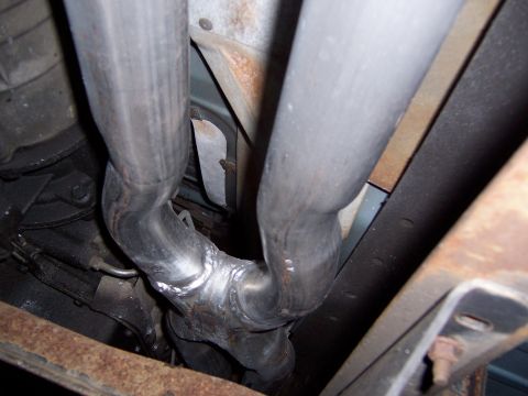 1995 Ford Bronco - Close-up view of the undercarriage of a vehicle, focusing on the exhaust system and rusted frame components.