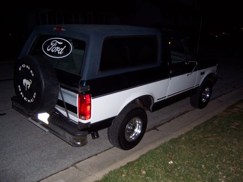 1995 Ford Bronco - Rear view of a two-tone 1995 Ford Bronco parked curbside at night.