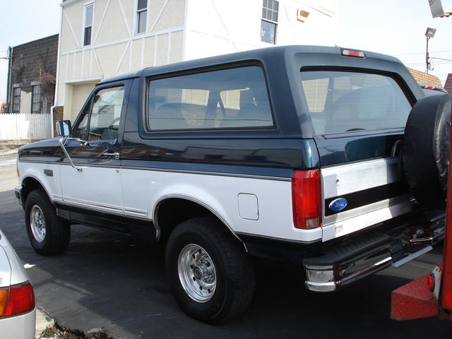 Dark green and white Ford Bronco SUV, rear three-quarter view, parked by a building