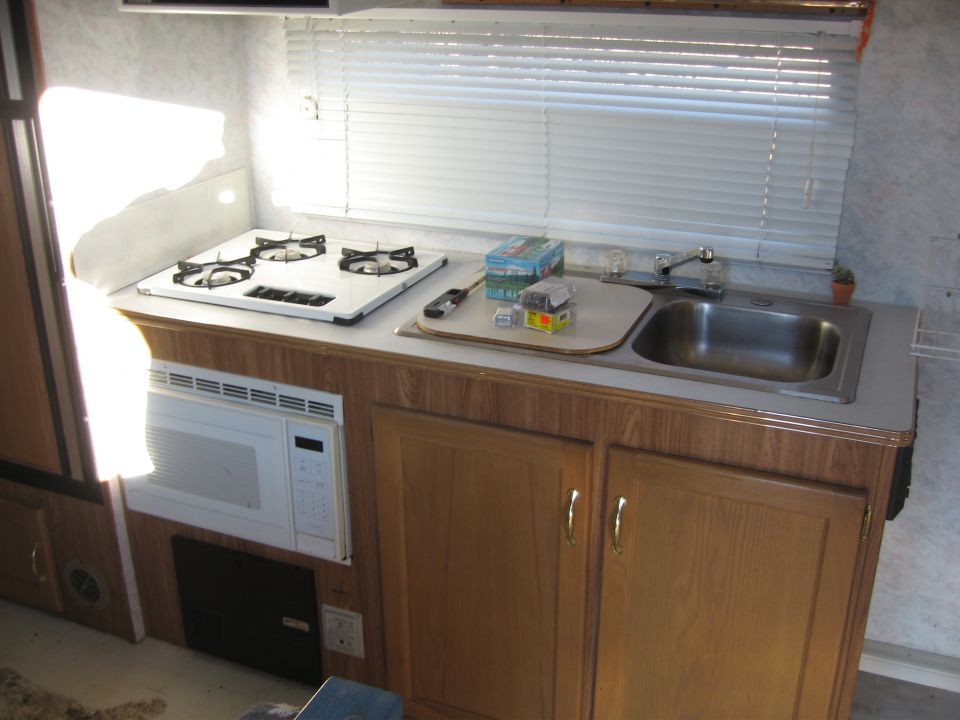 RV galley kitchen with three-burner propane cooktop, stainless sink and oak cabinets