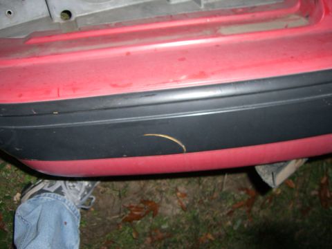 1988 Ford Bronco - Close-up of a red bumper with black trim, showing a scratch and a person's foot nearby.