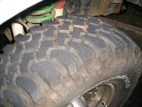 1989 Ford Bronco - A close-up view of an off-road tire and suspension components, including a green coil spring and red shock absorber.