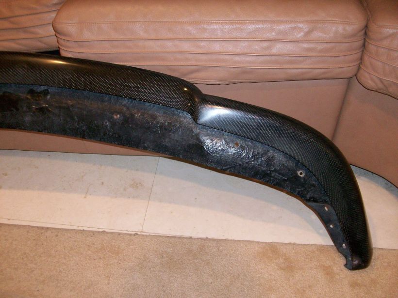 Carbon-fiber front lip spoiler with visible weave and unfinished backing on carpet