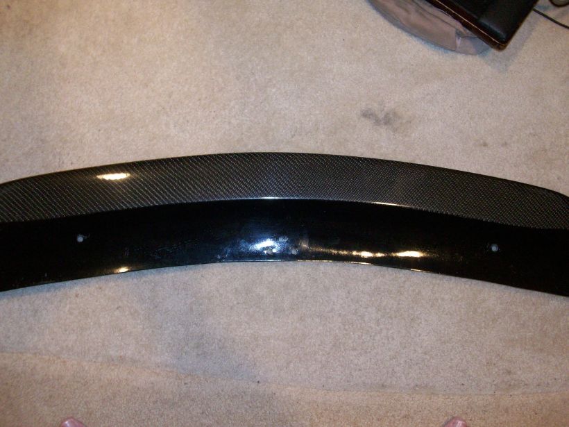 Carbon-fiber and gloss-black curved lip spoiler on carpet with mounting holes