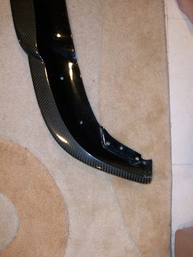 Carbon fiber front lip spoiler with mounting holes on a beige carpet