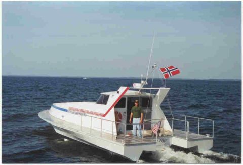 1978 Ford F-250 - A white catamaran boat navigates the water, with a person standing on its deck and a Norwegian flag flying from a mast.
