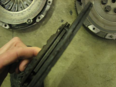 1995 Mitsubishi Eclipse - A hand holds a clutch disc assembly, with two flywheels visible in the background.