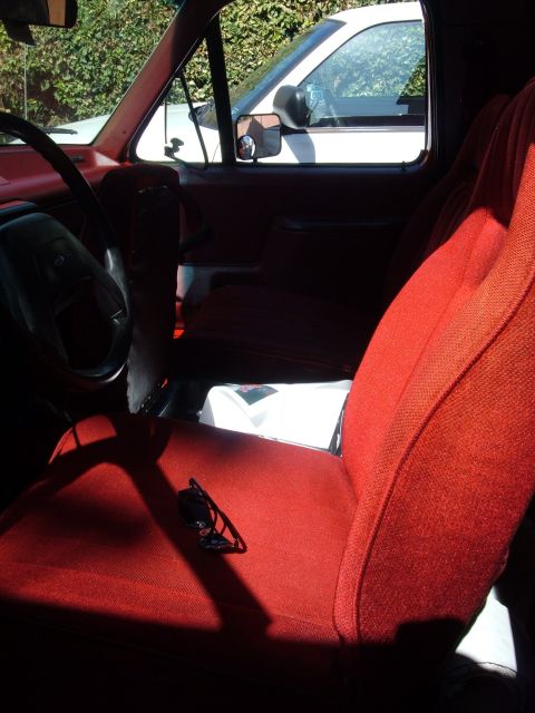 1988 Ford Bronco - Interior view of a truck's red seats and dashboard, with another vehicle seen through the window.