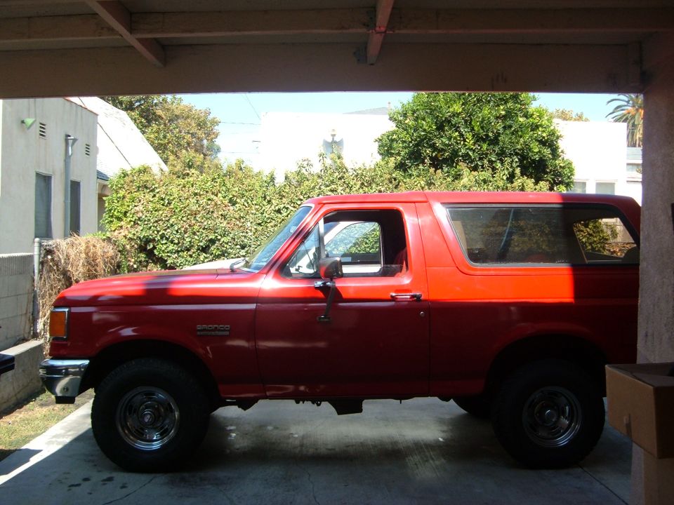 Driver-side view of a red Ford Bronco SUV parked under a carport