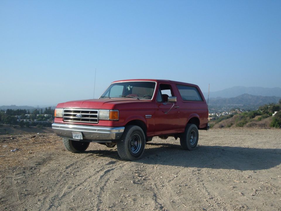 Red full-size Ford Bronco on a dirt hilltop with chrome bumper and black steel wheels