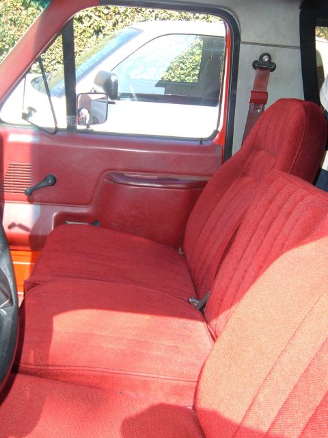 1988 Ford Bronco - Interior view of the front red cloth bench seat in a Ford truck/SUV, showing the driver's door panel with manual window crank, side mirror,…