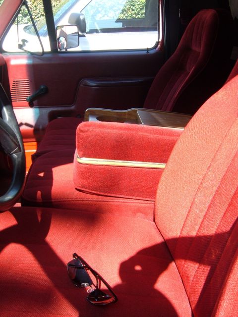 1988 Ford Bronco - Sunlit interior of a red-trimmed Ford truck cab shot from the passenger side, showing a red cloth split bench seat with a fold-down center…
