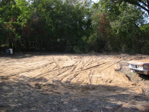 1996 Ford Bronco - The front end of a weathered orange vehicle is visible on the right side of the frame, parked on a dirt lot.