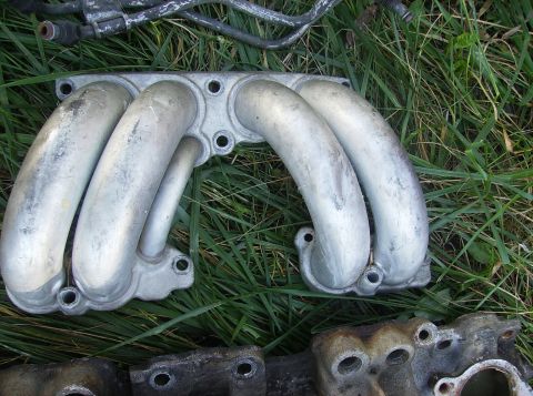 1995 Ford Probe - Aluminum intake manifold with four runners, part of an engine, placed on grass.