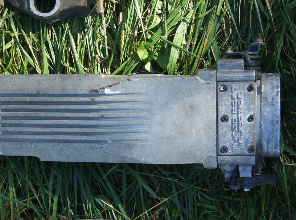 Aluminum automotive part with horizontal ridges and text 'TOP FEED INJECTOR' stamped on a metal plate