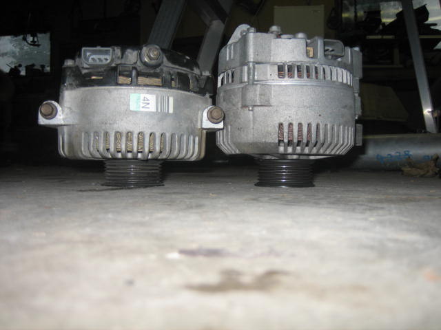 Two automotive alternators on a concrete floor. One has a blue and white sticker with '4N' visible