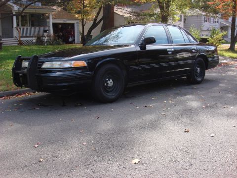 2003 Ford Crown Victoria - A black 2003 Ford Crown Victoria, equipped with a push bumper, is parked on a residential street.