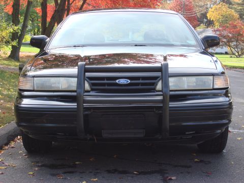 2003 Ford Crown Victoria - This black Ford Crown Victoria, likely a 1997 model, is equipped with a front push bar and is parked outdoors during autumn.