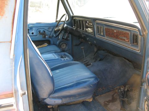 1979 Ford Bronco - The interior of a blue Ford Bronco shows worn seats and a wood-grain dashboard panel.