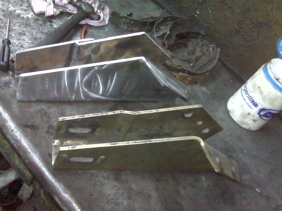 Metal brackets on a workbench with tools and a bottle