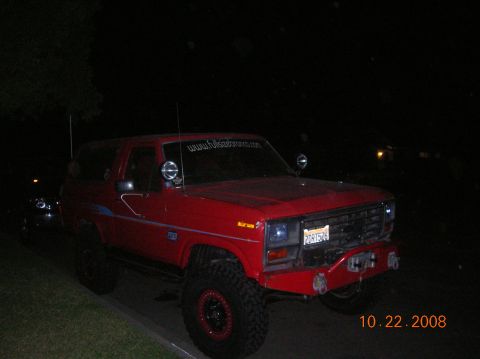 1985 Ford Bronco - A red Ford Bronco is parked on the side of the road at night, showing off its off-road modifications.