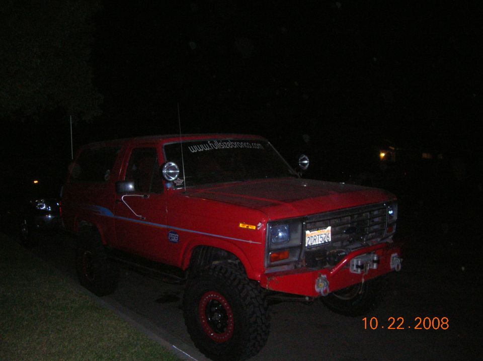 Red Ford Bronco with off-road tires and a winch, parked at night