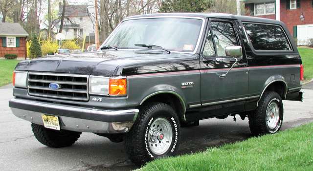 Black and gray Ford Bronco with chrome wheels parked on a grassy roadside