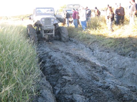 1990 Ford Bronco - Off-road vehicle attempts to navigate a muddy track, with onlookers present.