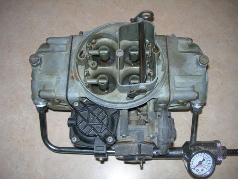 1985 Ford Bronco - A carburetor is shown with a connected fuel pressure gauge, indicating its function in fuel delivery systems.