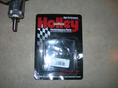 1985 Ford Bronco - A package of Holley performance parts sits on a textured surface next to a metal fitting.