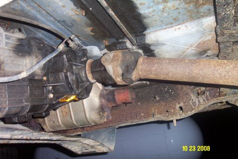 1992 Ford Bronco - The underside of a vehicle reveals its transmission, driveshaft, and exhaust components, showing signs of wear and leaks.