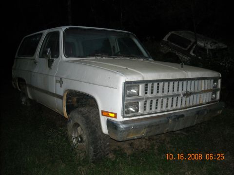 1979 Ford Bronco - White Chevrolet K5 Blazer with a prominent grille, parked outdoors at night. Another vehicle is visible in the background.