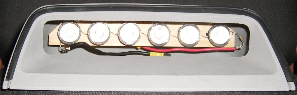 Car part with six circular lights wired on a wooden strip inside a gray housing