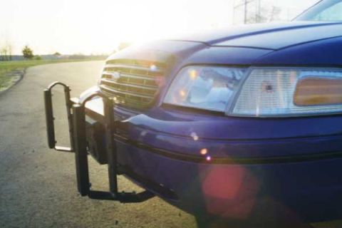1999 Ford Crown Victoria - Dark blue police car front end with push bar, seen from a low angle at sunset.
