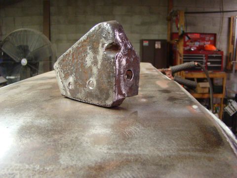 1948 Jeep Wrangler - A close-up of a metal component, possibly a bracket or mount, resting on a workbench in a workshop setting.