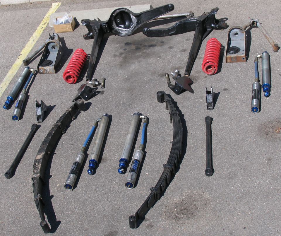 Various vehicle suspension parts laid out on pavement, including shocks, leaf springs, and a differential housing